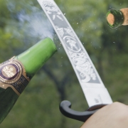 Garrafa de espumante tendo sua ponta arrancada com um sabre.